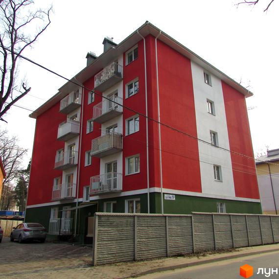 Житловий комплекс Щасливий: яскрава червоно-біла фасадна будівля з балконами та зеленою нижньою частиною. Огороджена територія з парканом та прилегла парковка.