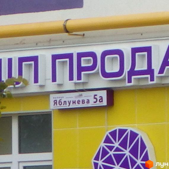 Новобудова ЖК Щасливий на Яблуневій, 5а. Зовнішній вигляд фасаду будівлі з фіолетовими літерами та жовтим оздобленням.