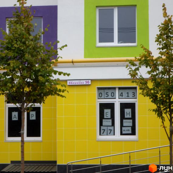 Житловий комплекс Щасливий на Яблуневій, 56. Фасад будинку з яскравими жовтими та зеленими елементами, вікнами з номерами квартир та деревами на прибудинковій території.