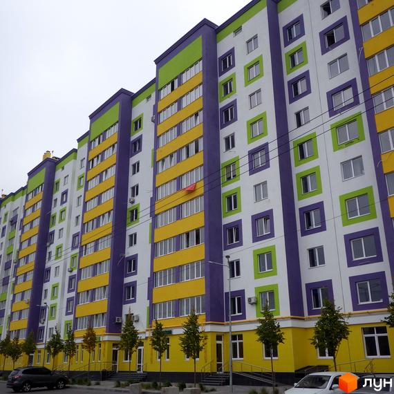 Житловий комплекс Щасливий на Яблуневій. Багатоповерховий будинок з фіолетовим, зеленим та жовтим фасадом. Поруч вулиця з деревами.