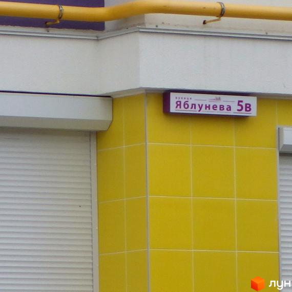 Житловий комплекс Щасливий на Яблуневій, 5В. Фасад будівлі оздоблений жовтою плиткою, поруч розташований білий ролет.