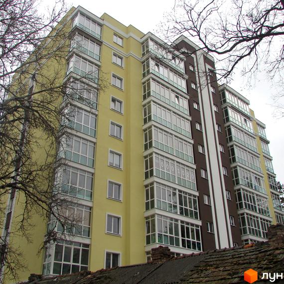 Житловий комплекс Полтавський: багатоповерховий будинок з жовтим та коричневим фасадом, скляними балконами та великою кількістю вікон. Навколо будівлі видно гілки дерев.