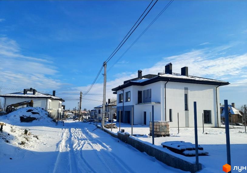 Котеджне містечко КМ ЗУБРА ETALON: білі двоповерхові будинки з чорними дахами та димарями, розташовані вздовж засніженої вулиці з слідами від техніки.
