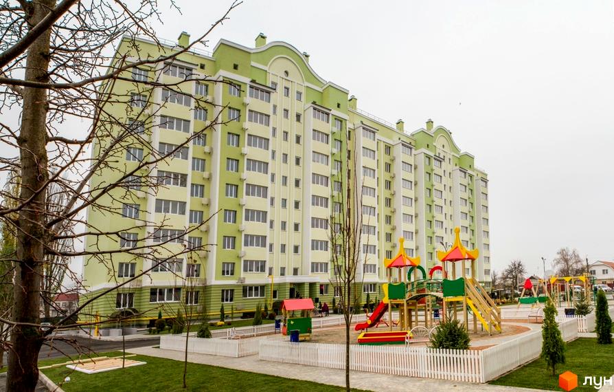 Житловий комплекс Первоцвіт з яскравим фасадом у світло-зелених тонах. На території комплексу дитячий майданчик та доглянута прибудинкова територія.