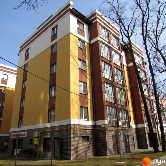 Зображення фасаду Житлового комплексу Затишний. Багатоповерховий будинок з жовтими та коричневими стінами, видно дерева.