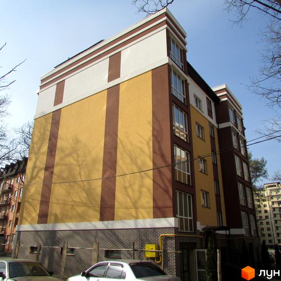 Зображення фасаду Житлового комплексу Затишний. Багатоповерховий будинок з жовтими та коричневими смугами, цегляний перший поверх.