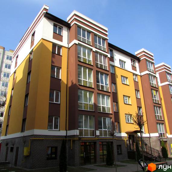 Зовнішній вигляд Житлового комплексу Затишний. Багатоповерховий будинок з жовто-коричневим фасадом та великими вікнами.