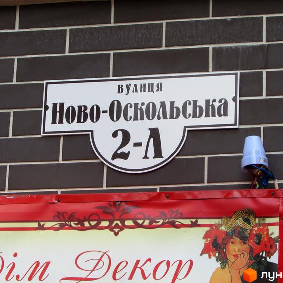 Вказівник адреси Житлового комплексу Затишний: вулиця Ново-Оскольська, 2-А. Білий знак з чорними літерами на темній цегляній стіні.