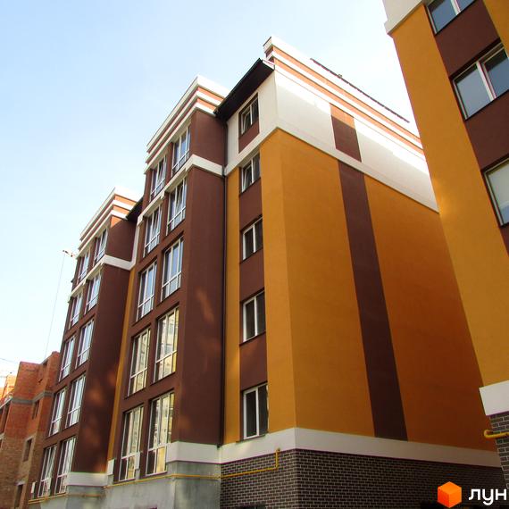 Фасад Житлового комплексу Затишний з коричневими та помаранчевими секціями, білими горизонтальними смугами. Видно вікна та цегляну основу.