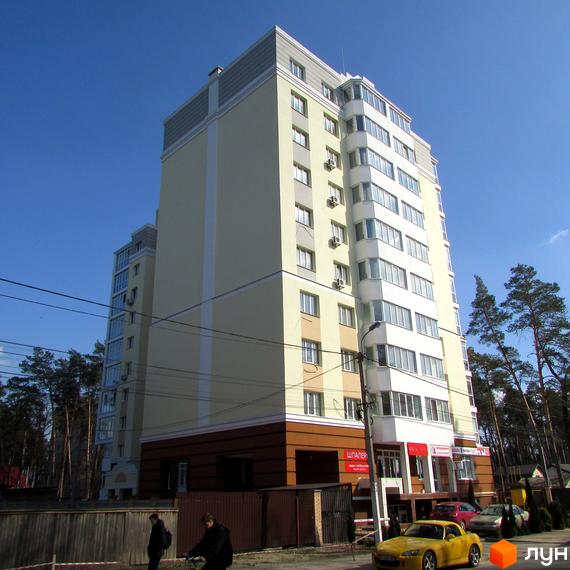 Зовнішній вигляд багатоповерхового житлового комплексу Капітал з жовтим фасадом та білими вікнами. Навколо будинку зелені насадження та припарковані автомобілі.