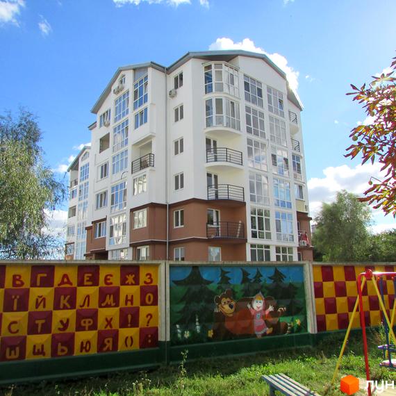 Житловий комплекс Вишиванка: біла багатоповерхівка з великою кількістю вікон та балконів. На прибудинковій території дитячий майданчик та огорожа з мультфільмами та алфавітом.