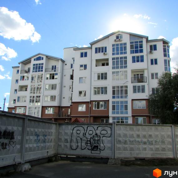 Новобудова ЖК Вишиванка з білою фасадною частиною та коричневим цоколем. Перед будинком розташована бетонна огорожа з графіті.