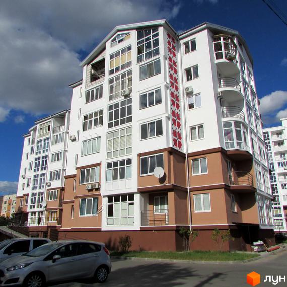 Житловий комплекс Вишиванка: фасади будівлі білого та коричневого кольору з великою кількістю вікон та балконів, перед будинком припарковані автомобілі.