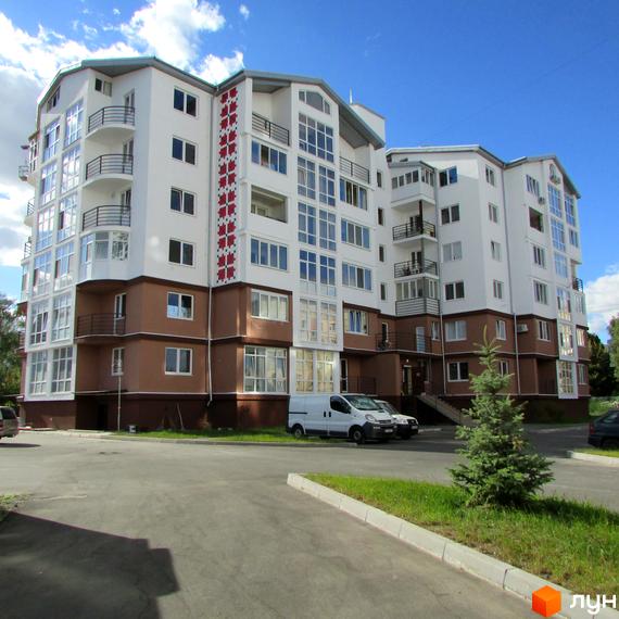 Житловий комплекс Вишиванка: багатоповерховий будинок з білими та коричневими фасадами, балконами та великими вікнами. Прибудинкова територія з парковкою та зеленими насадженнями.