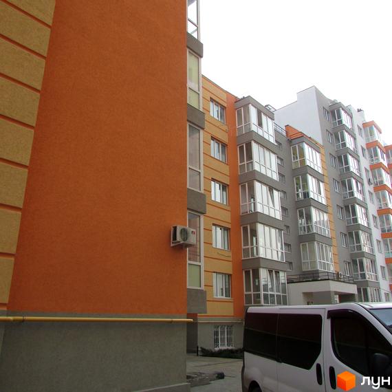 Зовнішній вигляд будинку ЖК Status з помаранчевим фасадом та сучасними вікнами. На прибудинковій території видно частину білого мінівену.