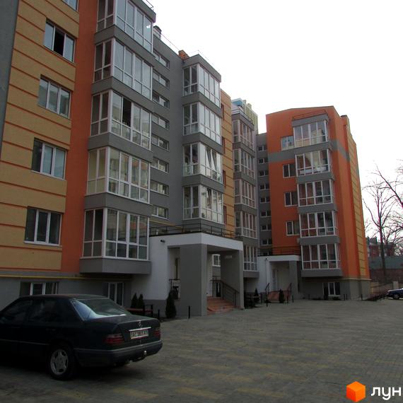 Зовнішній вигляд новобудови ЖК Status з сірими та помаранчевими фасадами, великою кількістю скління та прибудинковою територією з парковкою та зеленими насадженнями.