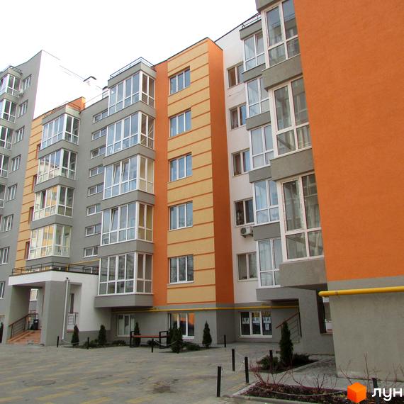 Зовнішній вигляд новобудови ЖК Status: багатоповерховий будинок з яскравим фасадом та заскленими балконами. На прибудинковій території розташовані зелені насадження та місця для відпочинку.