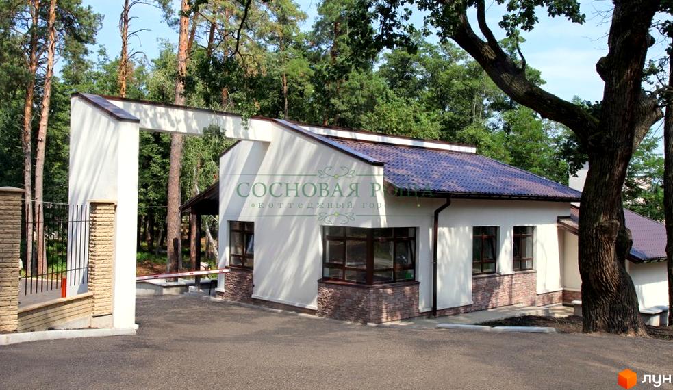 В'їзд до Котеджного містечка Соснова роща. Біла будівля з коричневим дахом та вікнами, оздоблена каменем. На території багато дерев.
