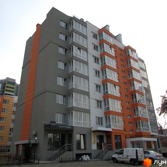 Житловий комплекс Status - багатоповерхова новобудова з помаранчевими та сірими фасадами, великими вікнами. Біля будинку розташована прибудинкова територія з парковкою.