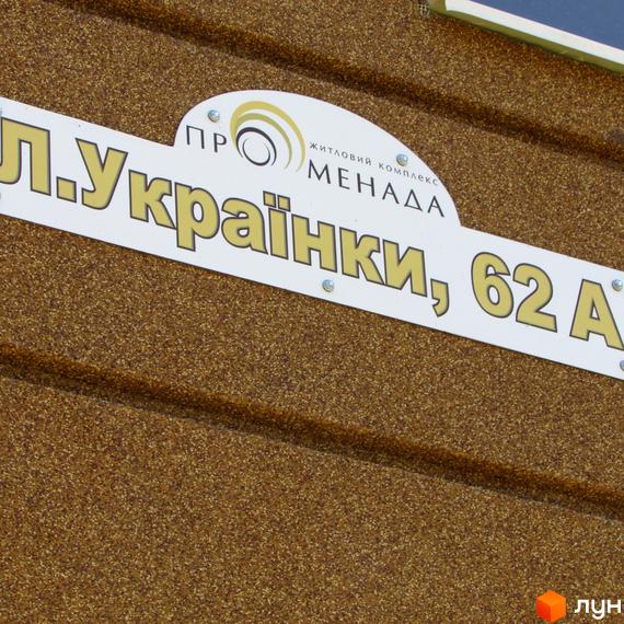 Фасад будівлі житлового комплексу Променада, виконаний з коричневого текстурованого матеріалу. На ньому розміщена табличка з адресою Л.Українки, 62 А.
