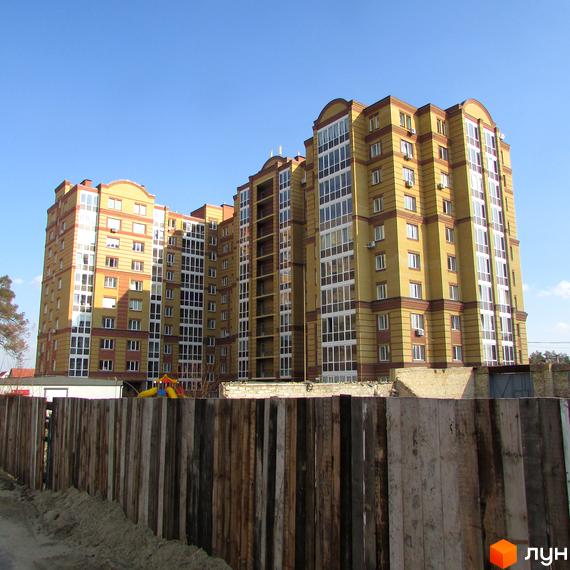 Висотна новобудова ЖК Центральний з фасадом у жовто-коричневих тонах на фоні блакитного неба. Перед будинком дерев'яний паркан.