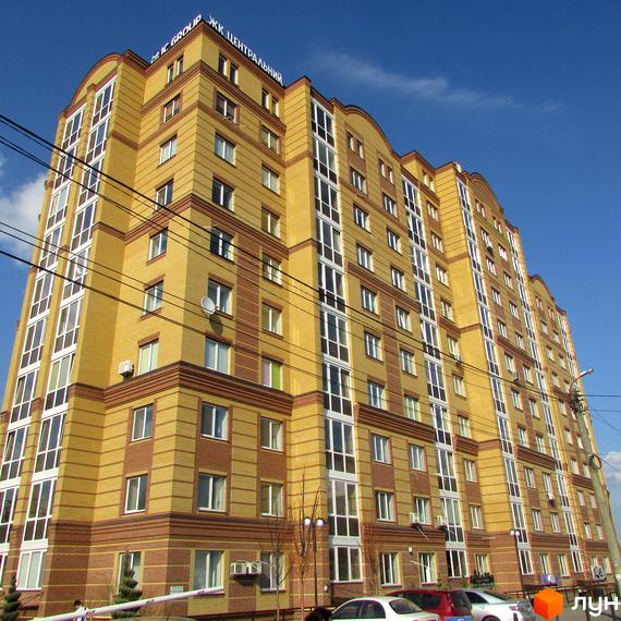 Висотна новобудова ЖК Центральний з жовтої цегли на тлі блакитного неба. На першому поверсі розташовані вікна та парковка.