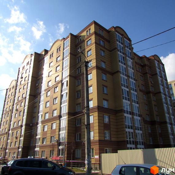 Висотна новобудова ЖК Центральний з цегляним фасадом та панорамними вікнами. На передньому плані припарковані автомобілі та огорожа.