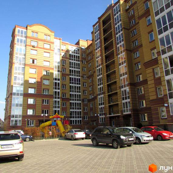 Висотна новобудова ЖК Центральний з великими вікнами та балконами. На прибудинковій території парковка та дитячий майданчик.