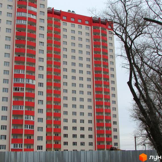 Висотна новобудова ЖК Олімпійський з червоними балконами. На передньому плані паркан, на задньому - дерева.