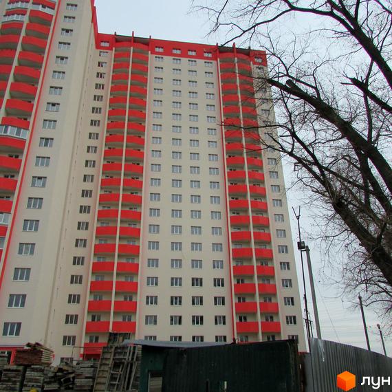 Висотна будівля житлового комплексу з червоними балконами. На передньому плані видно будівельні матеріали та дерева.