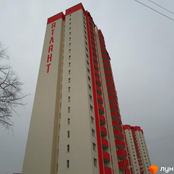 Висотна новобудова з червоними балконами та написом «АТЛАНТ» на фасаді. Сіре небо та відсутність прибудинкової території.