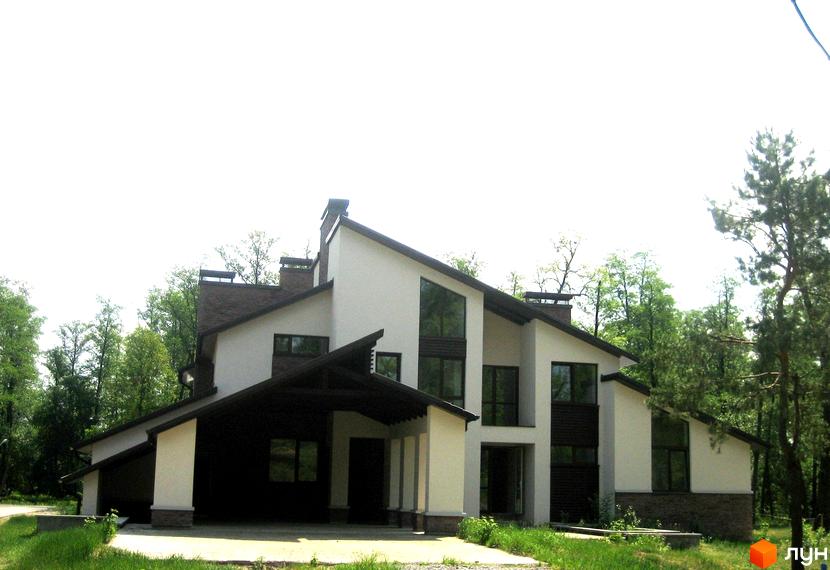 Будинок з білими стінами та темним дахом. На території багато зелені та дерев.