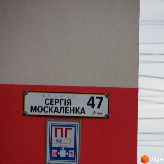 Вуличний знак з назвою вулиці Сергія Москаленка та номером будинку 47. На червоній стіні також розташовано інформаційний знак.