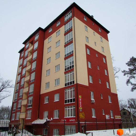 Висотна новобудова з червоними та бежевими фасадами. Біля будинку розташована кована огорожа та сніг.