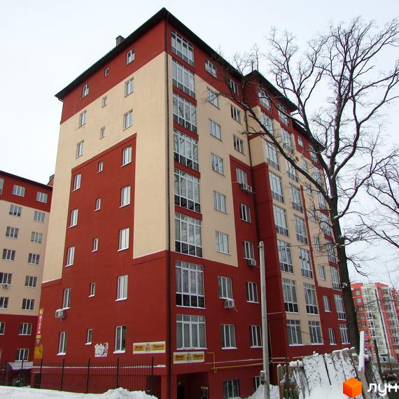 Багатоповерховий будинок ЖК Green Life з червоними та бежевими фасадами. На передньому плані огорожа та сніг.