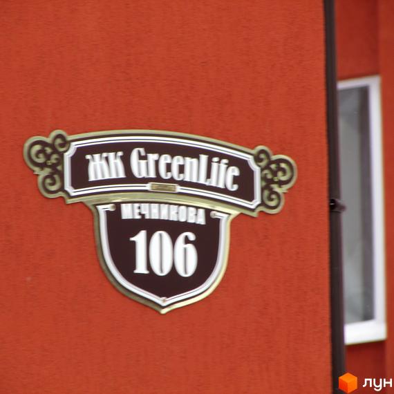 Вивіска ЖК GreenLife з номером будинку 106 на червоній стіні. На вивісці також вказана назва вулиці - Мечникова.