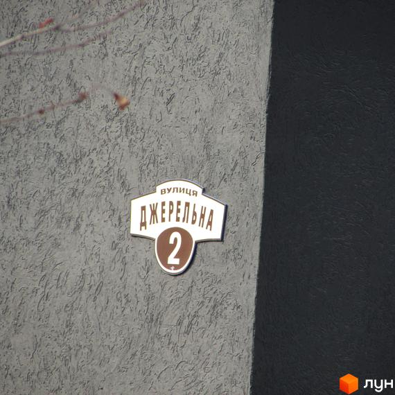 Вуличний знак з назвою вулиці «Джерельна» та номером будинку 2 на фоні фасаду будівлі. Поруч розташована частина темного фасаду.