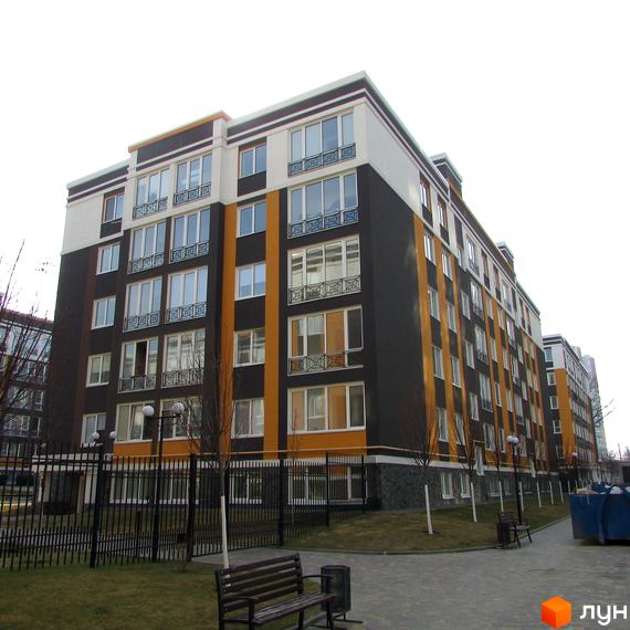 Багатоповерхова новобудова ЖК Фортуна-2 з великими вікнами та балконами. На території є лавки, смітники та огородження.