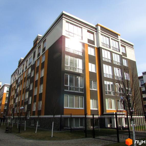Багатоповерховий будинок ЖК Фортуна-2 з великими вікнами та комбінацією кольорів на фасаді. На території є газон, дерева та кована огорожа.