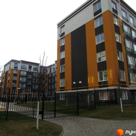 Житловий комплекс Фортуна-2 з фасадом у помаранчевих та чорних тонах. На території є газон, дерева та кована огорожа.