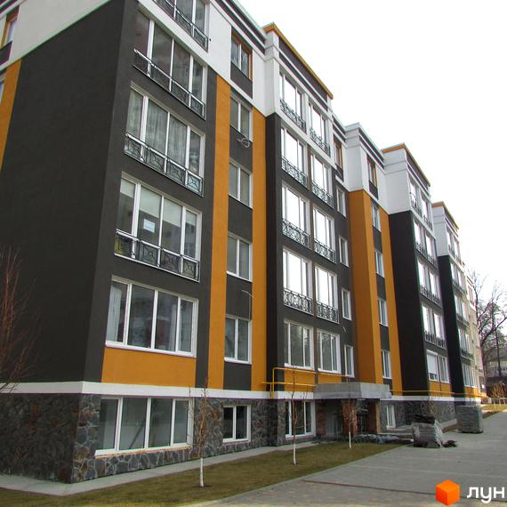 Зовнішній вигляд багатоповерхового будинку ЖК Фортуна-2 з темним фасадом та жовтими вставками. На першому поверсі оздоблення каменем, поруч доглянута прибудинкова територія.
