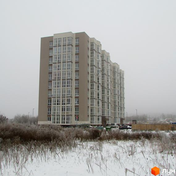 Висотна новобудова ЖК Ярославський взимку. Фасад будівлі з великою кількістю вікон, перед будинком засніжена територія з рослинністю.