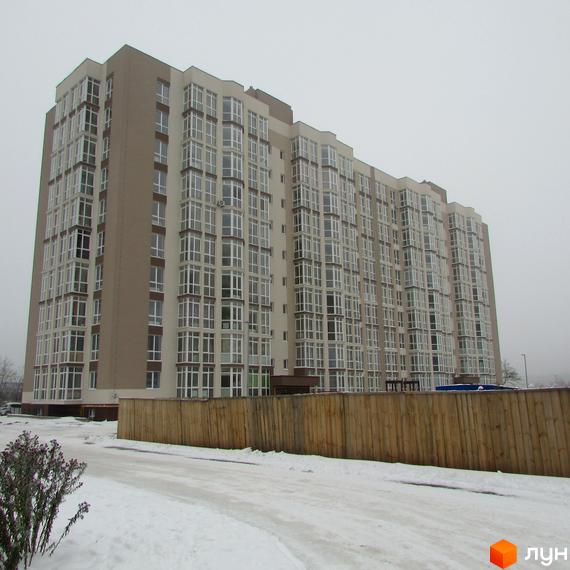 Висотна будівля ЖК Ярославський з великою кількістю вікон на тлі засніженої місцевості. На передньому плані дерев'яний паркан та дорога.