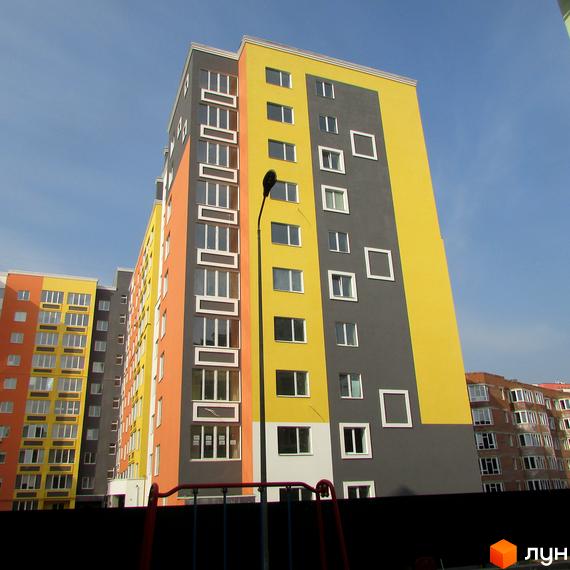 Багатоповерховий будинок ЖК Синергія-2 з яскравим фасадом у жовто-сірих тонах. На передньому плані ліхтар та частина дитячого майданчика.