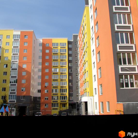 Яскравий багатоповерховий будинок житлового комплексу Синергія-2 з різнокольоровими фасадами. На території є дитячий майданчик та парковка.