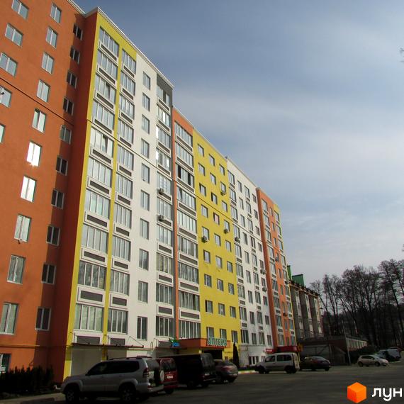 Багатоповерховий будинок ЖК Синергія-2 з різнокольоровими фасадами. На прибудинковій території припарковані автомобілі.