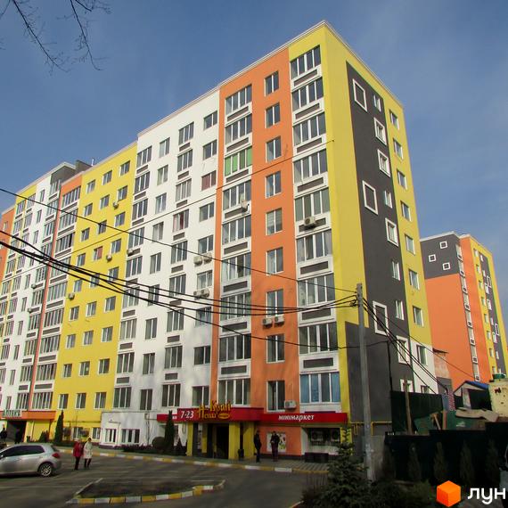 Багатоповерхова новобудова ЖК Синергія-2 з яскравим фасадом. На прибудинковій території є парковка та зелені насадження.