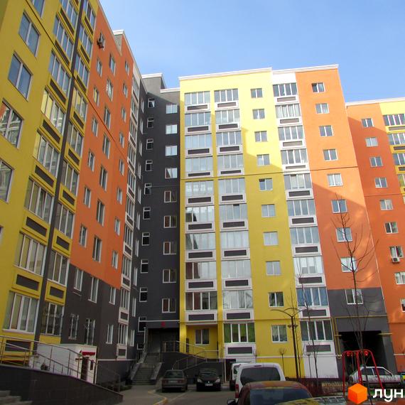 Багатоповерховий будинок ЖК Синергія-2 з яскравим фасадом. На прибудинковій території є парковка та дитячий майданчик.