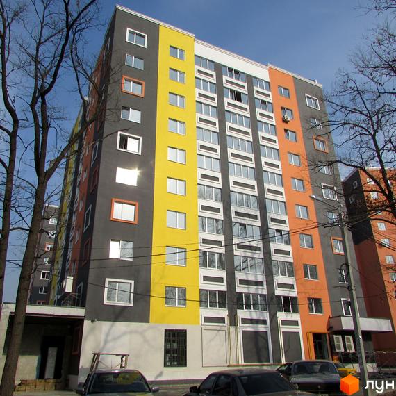 Багатоповерховий будинок житлового комплексу Синергія-2 з яскравим фасадом. На передньому плані припарковані автомобілі, а також видно дерева.