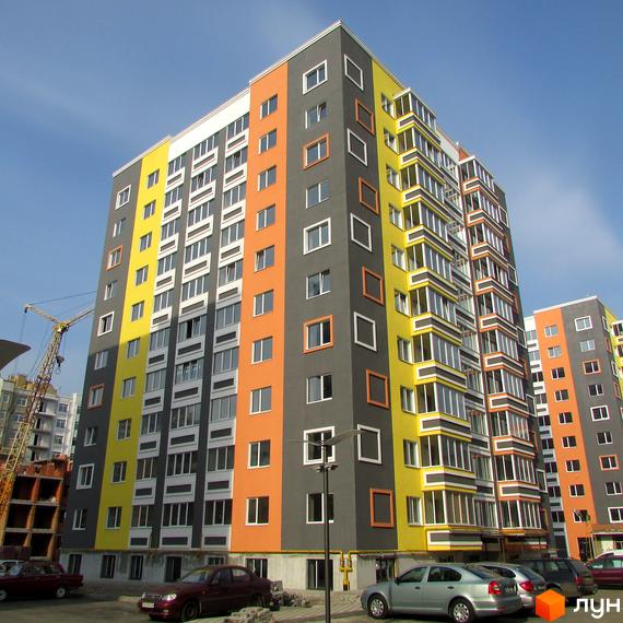 Багатоповерховий будинок житлового комплексу Синергія-2 з яскравим фасадом. На прибудинковій території припарковані автомобілі.